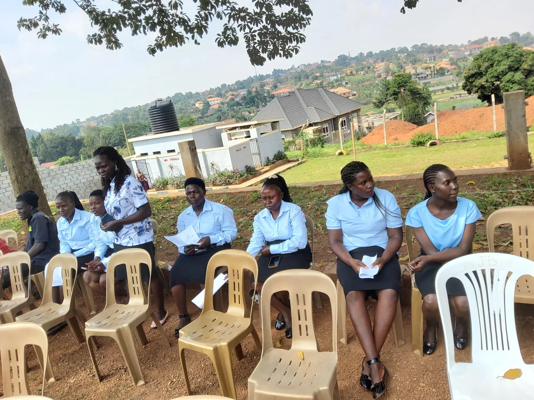 Members of staff in pale blue and white seated beneath trees near the audience area