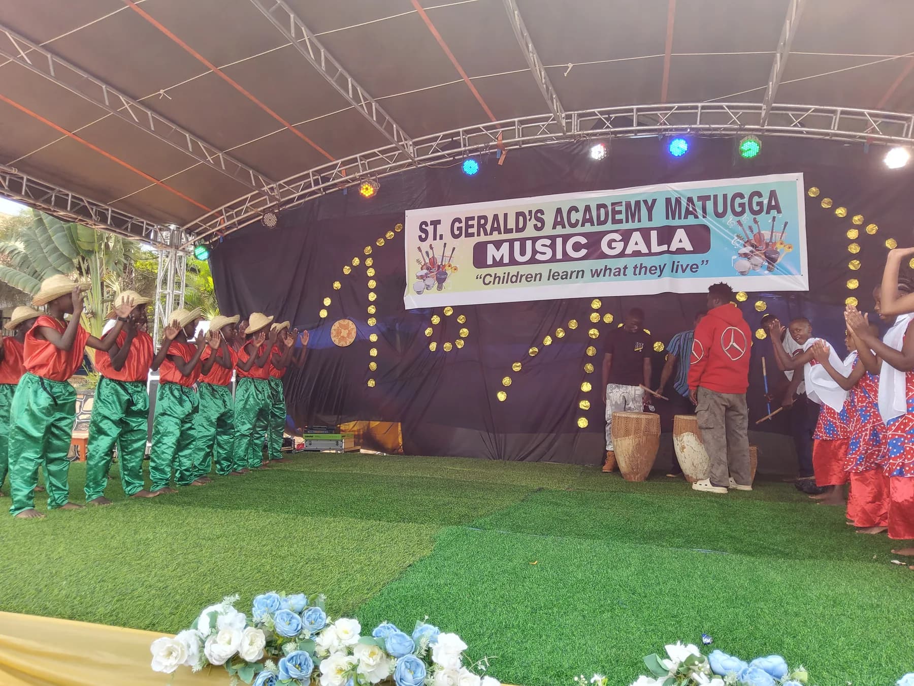 Two groups of learners facing each other in colourful costumes beside traditional drums