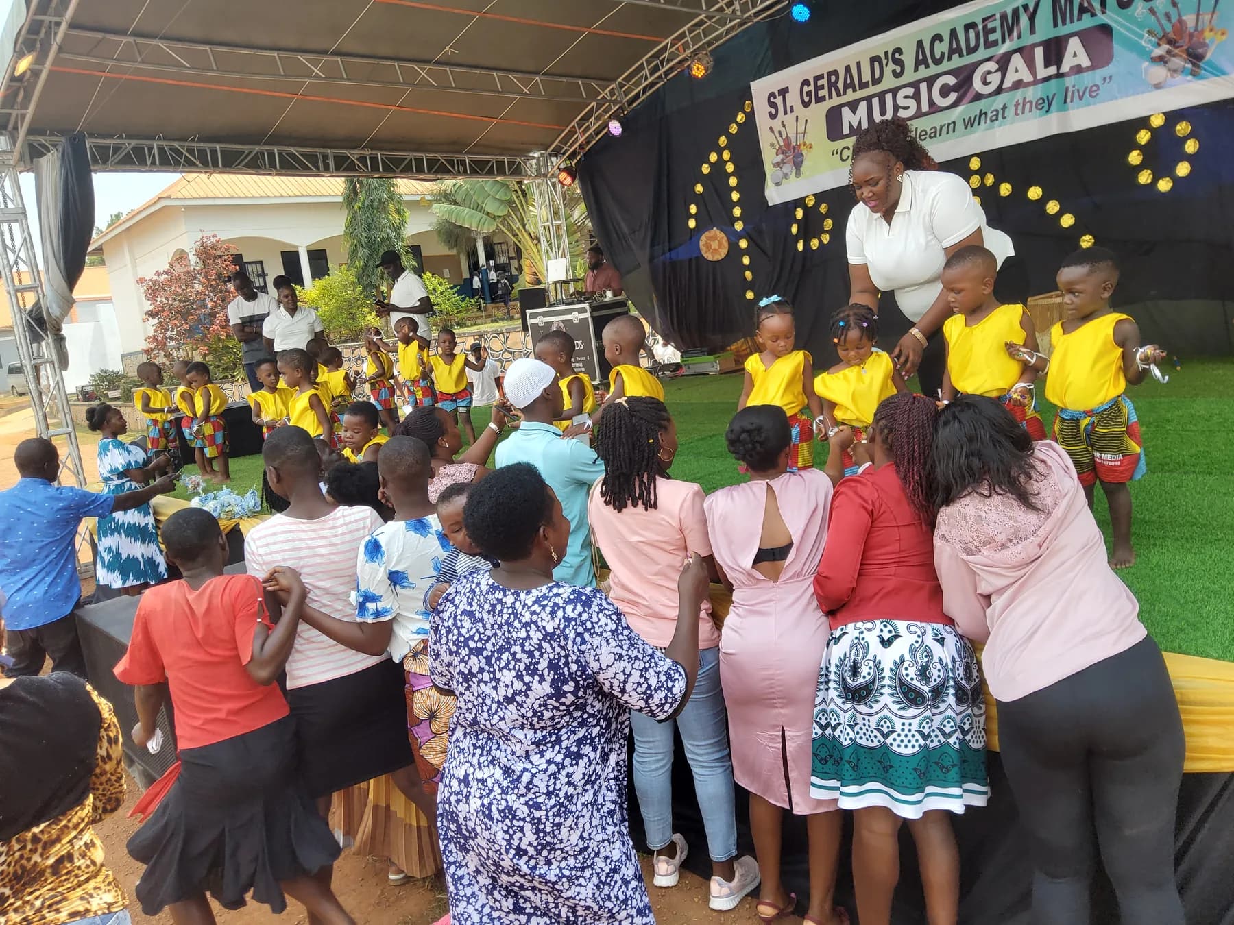 Families gathered at the stage while a teacher helps young performers in yellow costumes