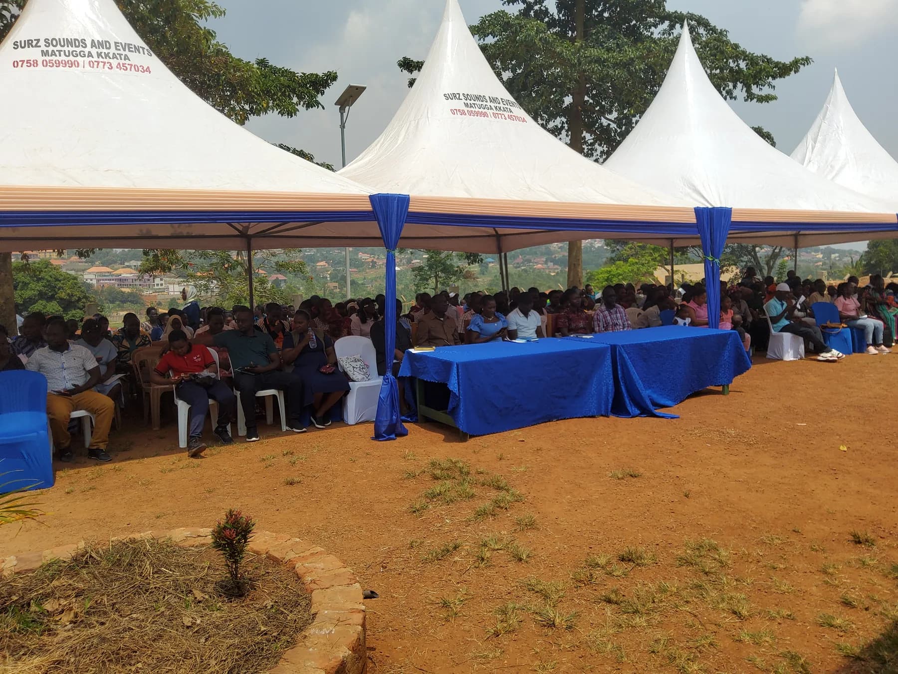 A wide view of the audience seated beneath connected white event tents