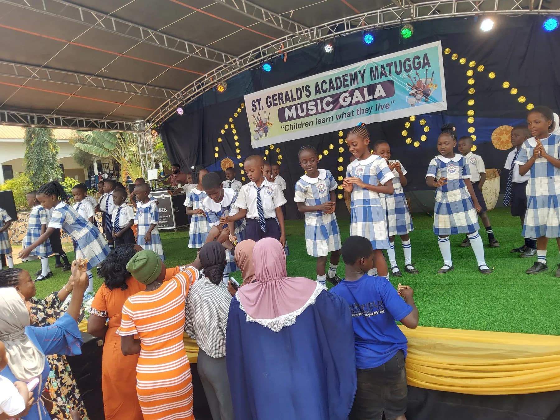Uniformed pupils smiling and reaching toward supporters gathered at the front of the stage