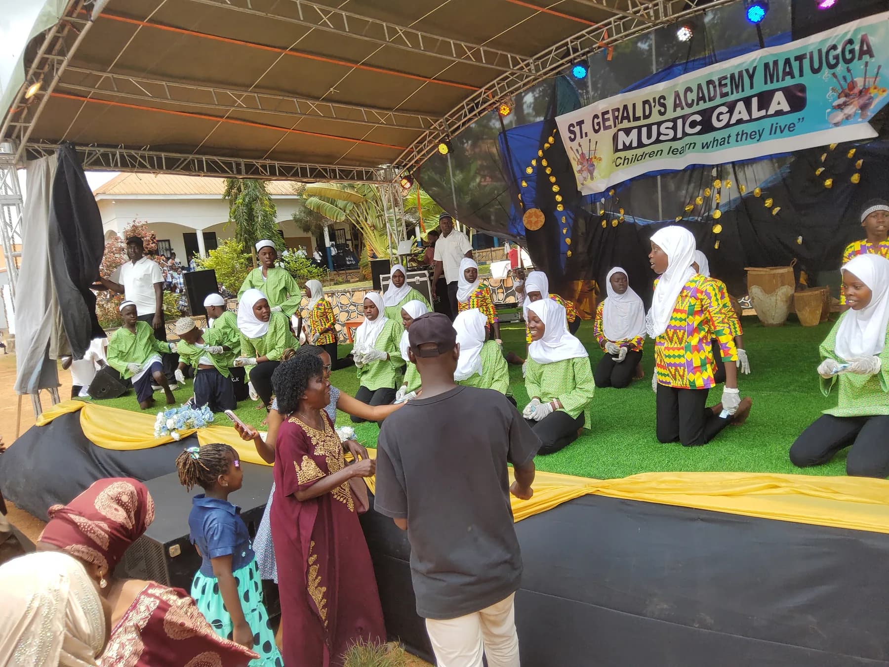 The green-and-white performance group kneeling on stage as families watch from close by