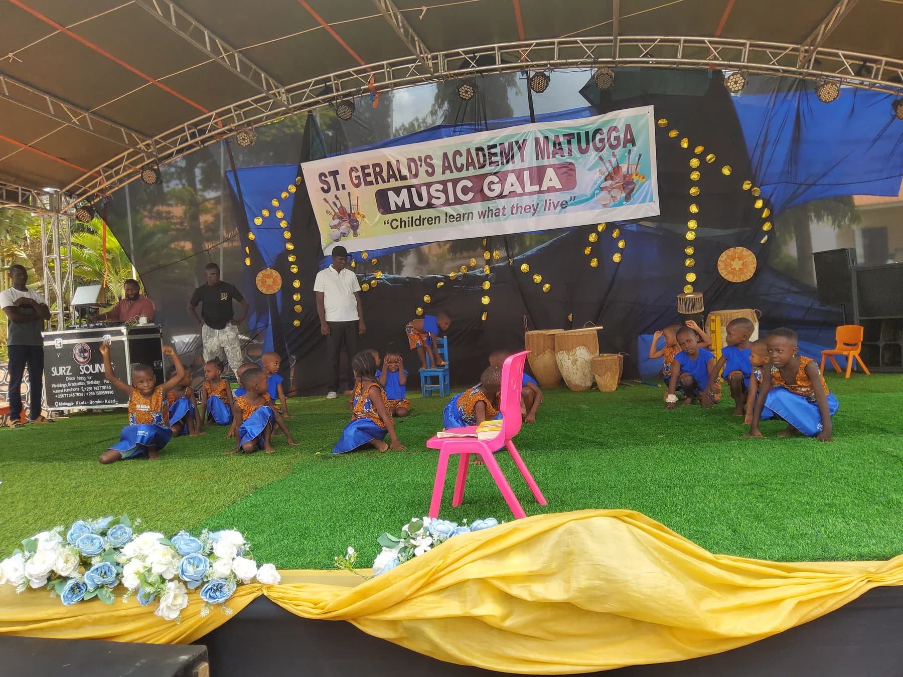 A young performer using stacked blue chairs as classmates hold a low stage formation