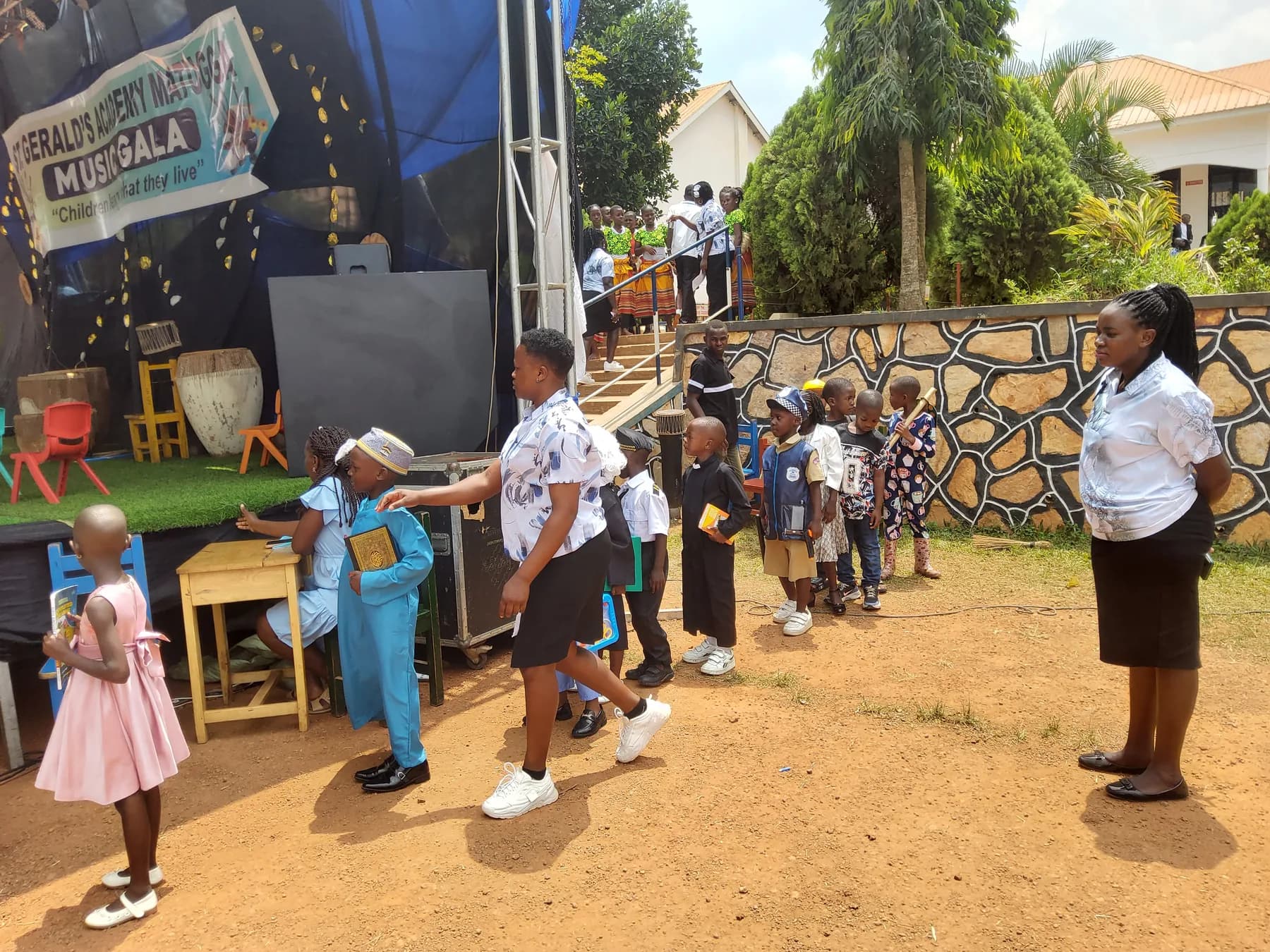 Children in career-themed costumes carrying books and props while waiting beside the stage
