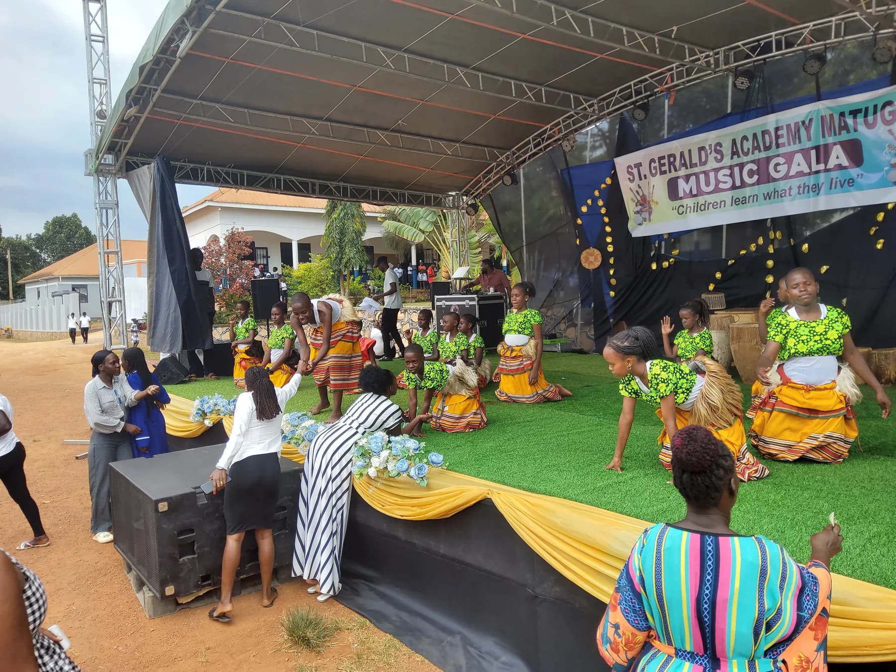 Traditional dancers kneeling near the front of the stage while supporters reach up to greet them