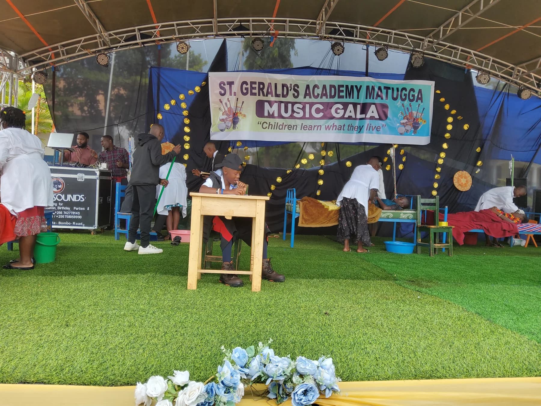 Pupils acting in a multi-scene drama with a desk, beds, basins and colourful chairs