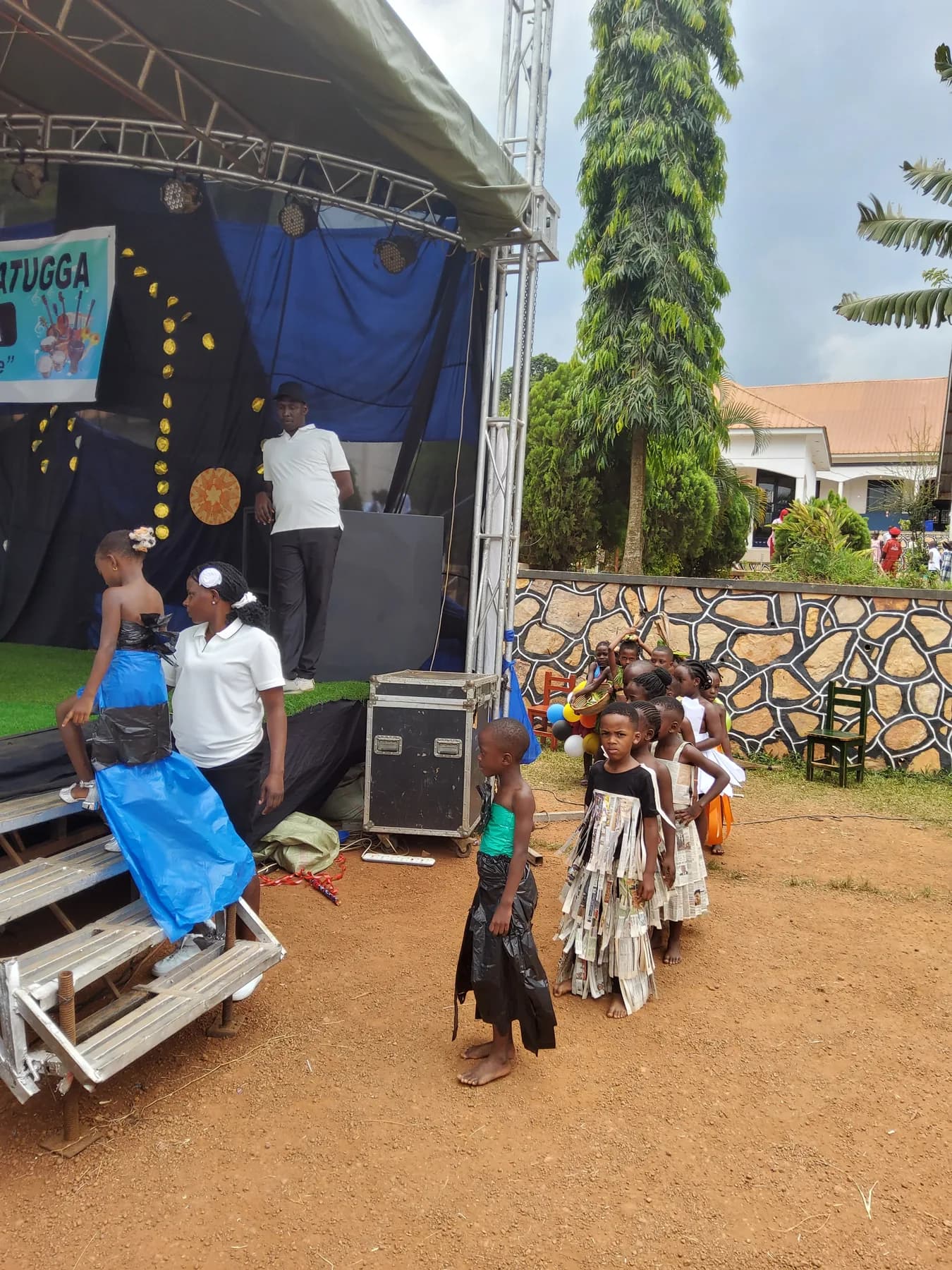 Children in costumes made from blue plastic, newspaper and other reused materials queuing beside the stage