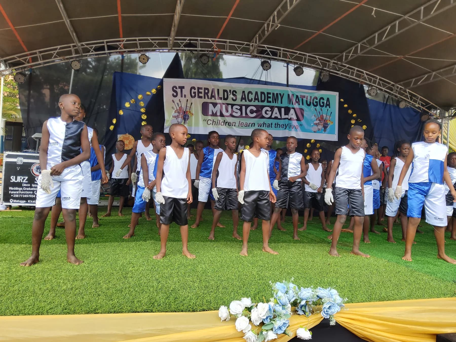 A large group of learners in blue, black and white satin outfits standing in performance formation