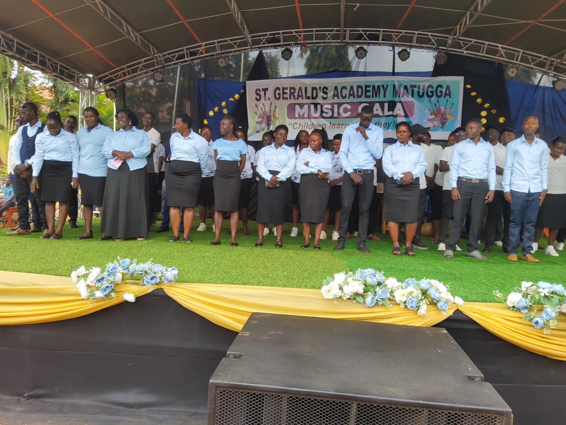 Staff members in pale blue shirts and dark skirts or trousers standing together on stage