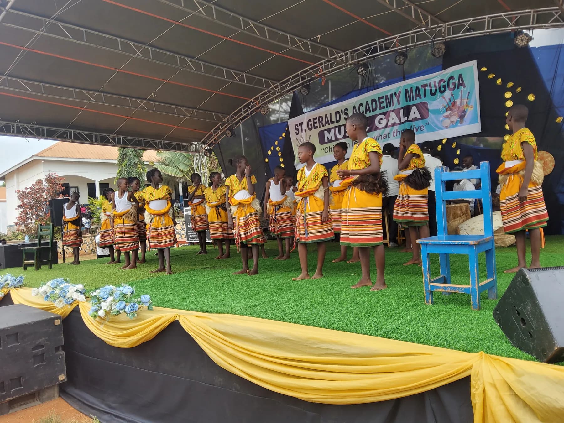 Learners in yellow tops, striped wrap skirts and traditional waist accents standing in formation