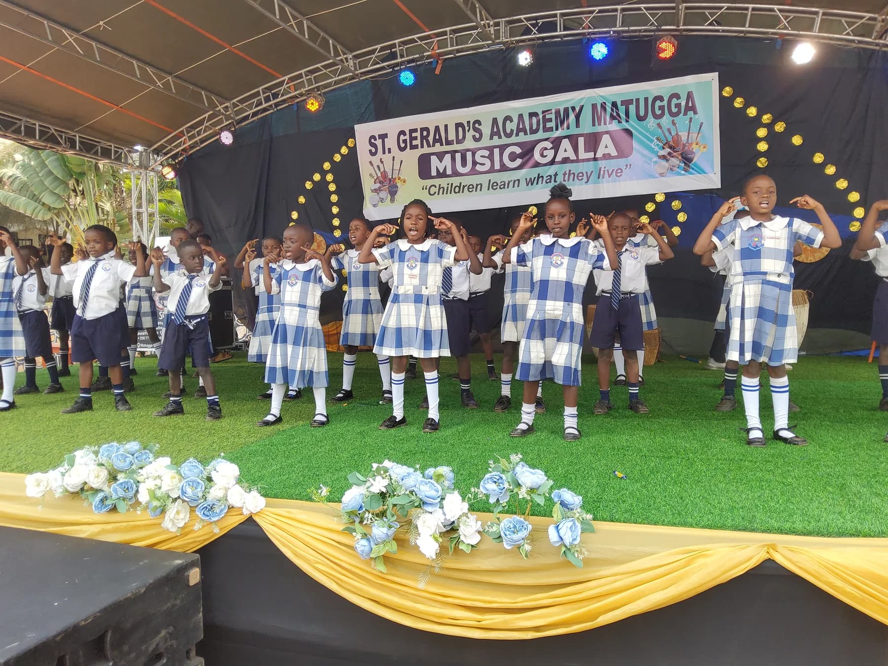 Primary pupils in school uniform singing and performing coordinated hand movements