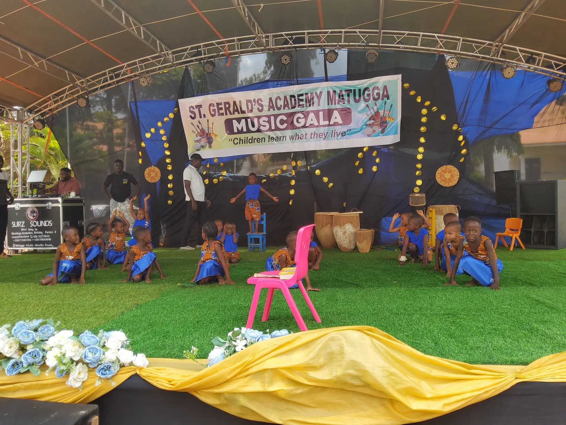 Young learners in blue-and-orange costumes performing with colourful child-sized chairs