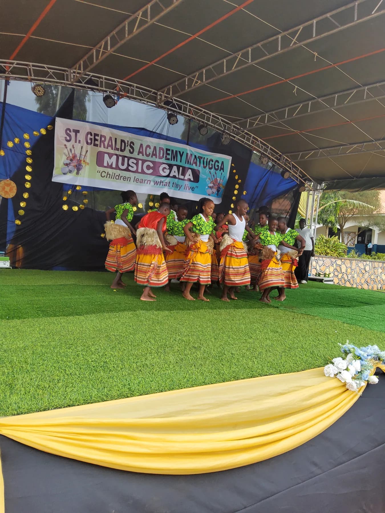 Learners in bright green tops and striped traditional skirts dancing together on the Music Gala stage