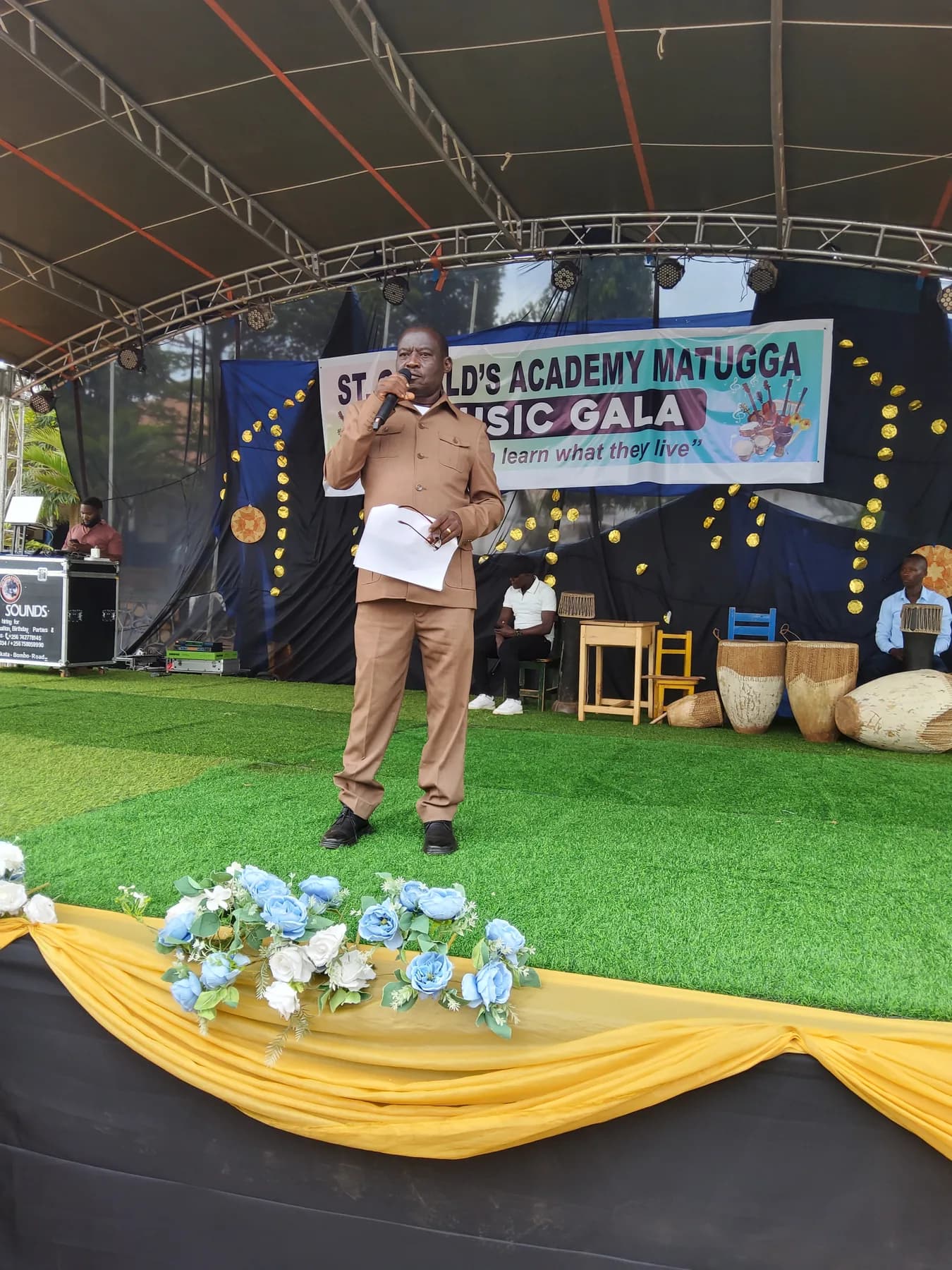 Guest of Honour Mr. Mwesige Paul speaking into a microphone on the Music Gala stage